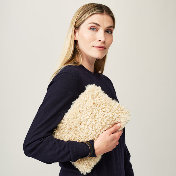 Model holding cream faux sheepskin clutch bag with leather wrist strap by Helen Moore