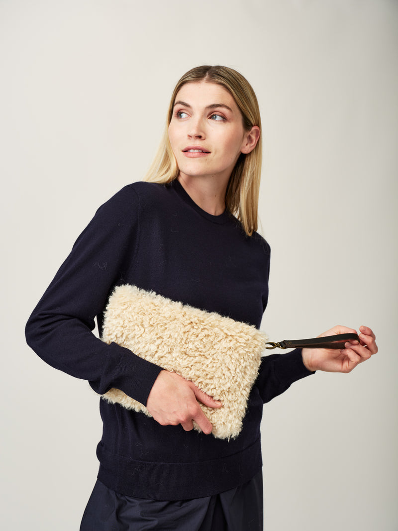 Model holding cream faux sheepskin clutch bag with leather wrist strap by Helen Moore