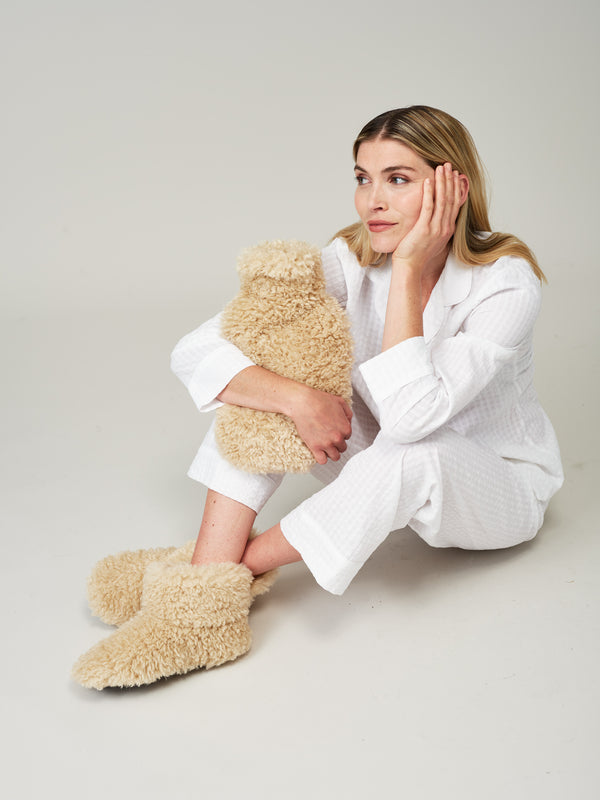 Model wearing Cream faux sheepskin Slipper Boots by Helen Moore and holding a hot water bottle